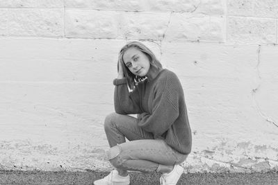 Portrait of smiling young woman sitting against wall