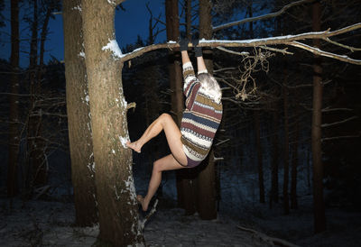 Woman standing by tree trunk in forest