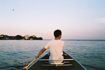 Rear view of man rowing boat in sea during sunset