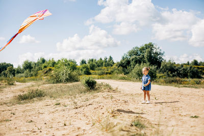 A little girl is flying a kite on a field road outside the city. childhood, joy, care