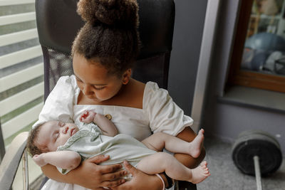 Girl holding baby sister on chair at home