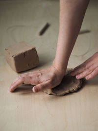 Young woman prepares clay to create a mug on a wooden table. 