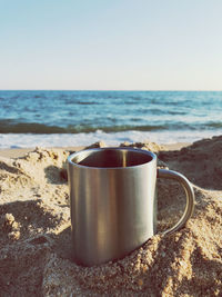 Close-up of coffee cup on beach against clear sky