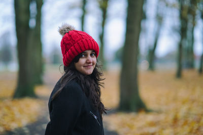 Portrait of smiling woman wearing knit hat against trees during autumn