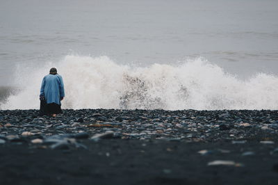 Rear view of woman by waves splashing in sea