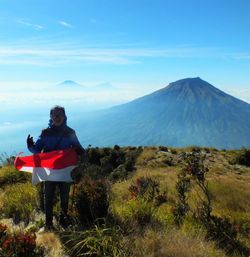 Portrait of man holding indonesian flag against mountain 