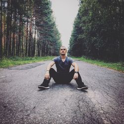 Portrait of young man sitting on road in forest