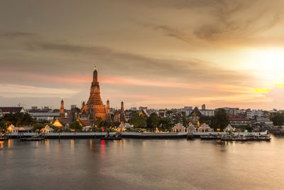 River amidst buildings against sky during sunset