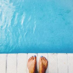 Low section of woman standing at poolside on sunny day