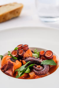 Stewed octopus squid with tomatoe sauce in a plate with bread and water glass