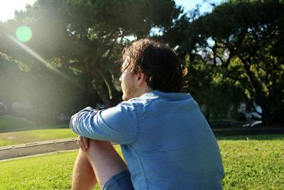 Side view of thoughtful man looking away while sitting on grassy field in park during sunny day