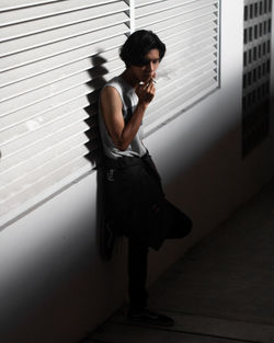 Young man smoking cigarette while leaning on wall