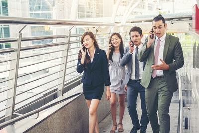 Colleagues using phones while walking on elevated walkway 