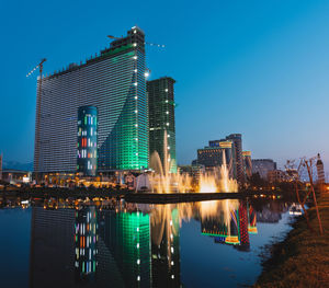 Illuminated buildings by river against clear sky