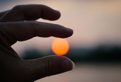 Close-up of hand holding sun during sunset