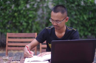 Man writing in paper while sitting outdoors