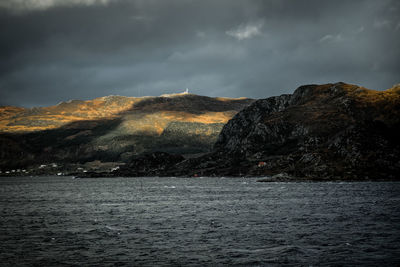 Scenic view of sea by mountain against storm clouds