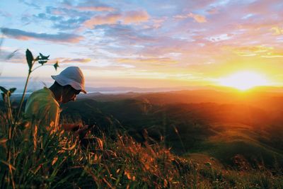 Man sitting on grass against sky during sunset