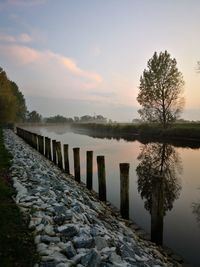 Wooden posts on lake against sky during sunset