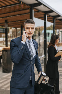 Businessman talking on smart phone while waiting at bus stop