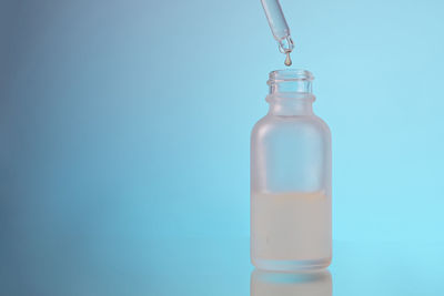 Face serum oil drop with dropper glass bottle pipette on blue background close up