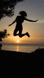 Silhouette man jumping in sea against sky during sunset
