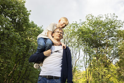 Father carried little child, son on shoulder while walking in park. summer time. happy parenthood