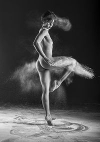 Naked woman dancing against black background