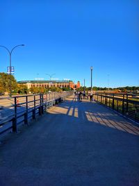 People walking on footpath against clear blue sky