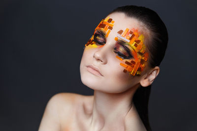 Close-up of shirtless young woman with eye make-up and rhinestones against gray background