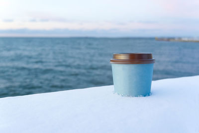 Close-up of coffee cup by sea against sky