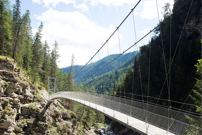 Footbridge amidst mountains against sky during sunny day