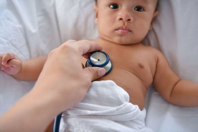 Cropped hand of female doctor examining shirtless baby boy on bed