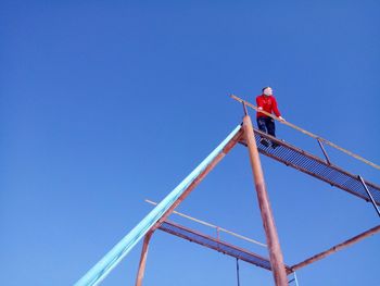 Low angle view of man working at construction site against clear blue sky