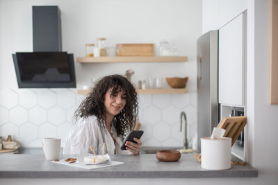 Young woman using phone while sitting on table at home