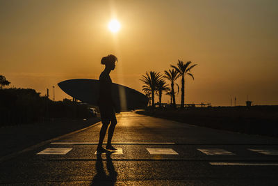 Silhouette of an african american surfer walking at sunrise with surfboard