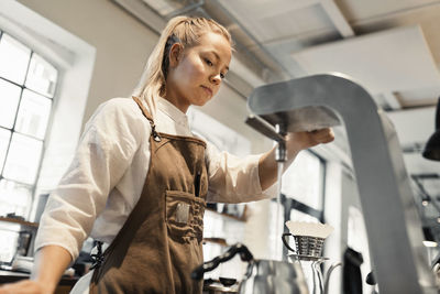 Young female barista pouring boiling water in coffee pot from machine at cafe