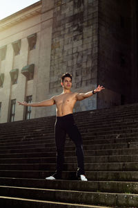 Full length of shirtless man standing against staircase