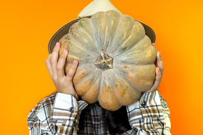 Midsection of woman holding pumpkin against yellow background