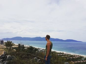 Man looking at sea while standing on mountain against cloudy sky