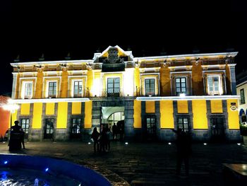 People on illuminated street against buildings at night