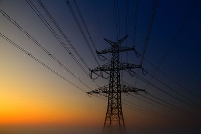 Low angle view of electricity pylon against sky during sunset