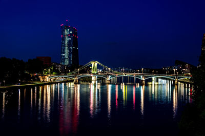 Illuminated bridge over river by buildings against sky at night