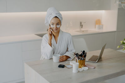 Smiling woman with eye patch talking on phone while holding coffee cup at home