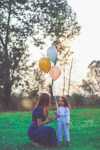 Girl with balloons on field by trees