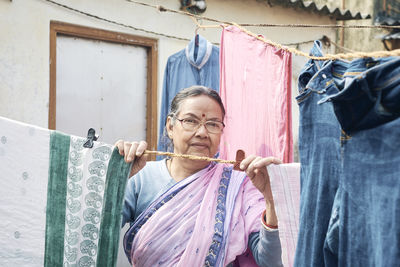 Portrait of a simple looking mature indian woman hanging freshly washed laundry to dry in the sun