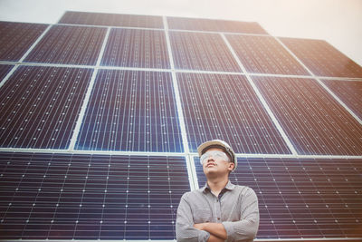 Low angle view of man with arms crossed standing against solar panels