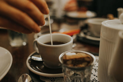 Cropped image of hand pouring milk in coffee cup at table