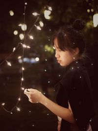 Side view of girl standing by illuminated lights