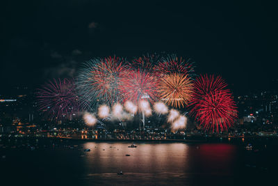 Firework display over illuminated city against clear sky at night